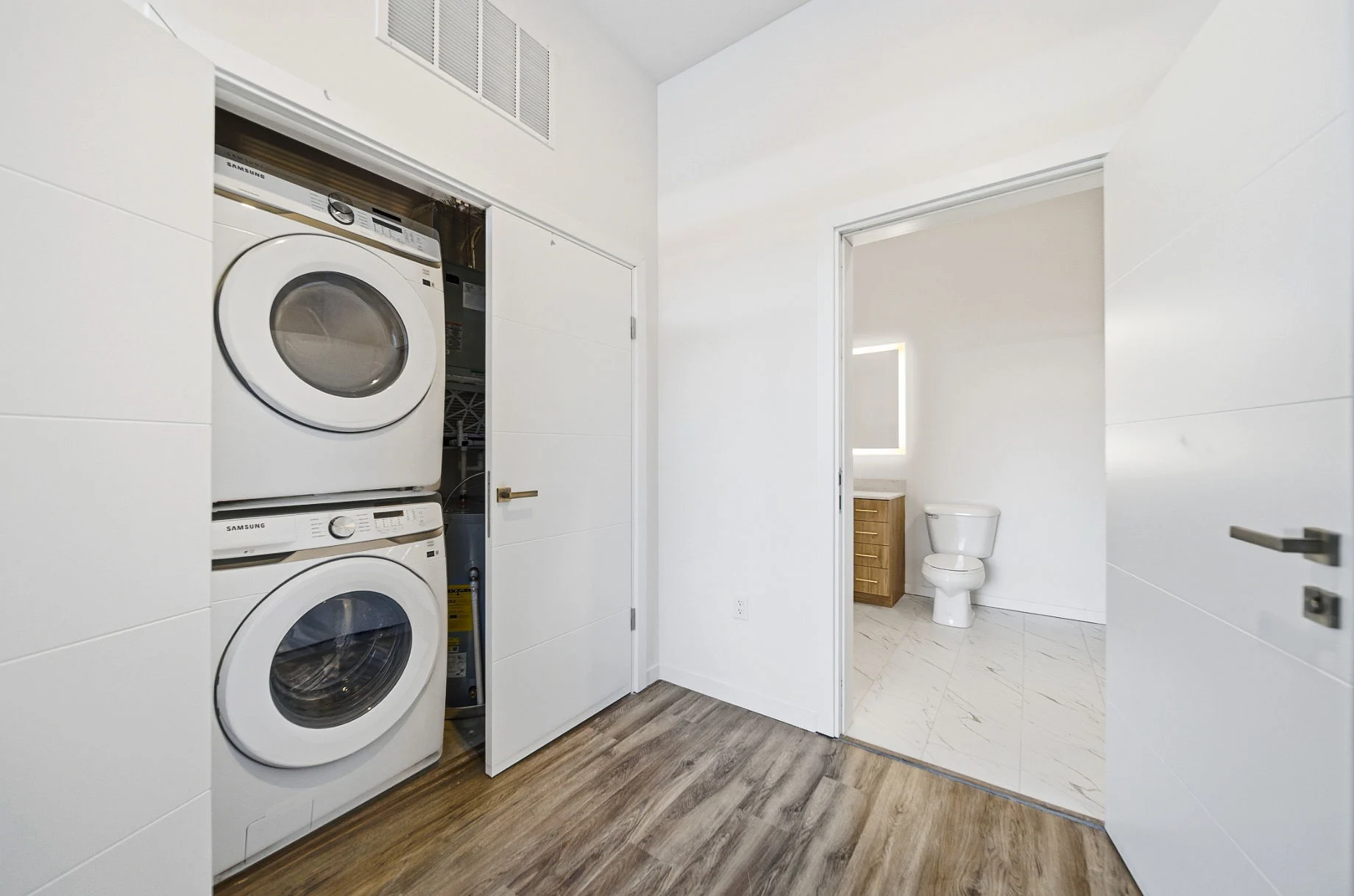 In-unit stacked washer and dryer beside a bathroom with a backlit mirror at Webster Station Flats